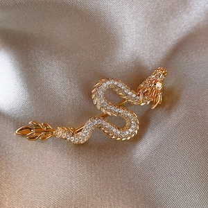 Macro detail of a gold-plated dragon brooch with white cubic zirconia on silk