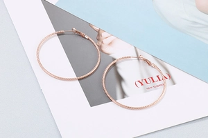 Detailaufnahme der roségoldenen Creolen mit gewebter Textur auf Lifestyle-Hintergrund