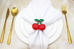 Close-up of vibrant red cherry napkin rings with green leaves on white napkins