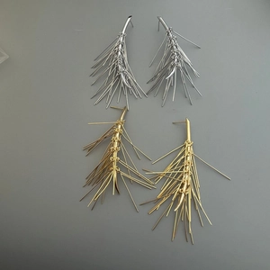 Dettaglio degli orecchini a nappa ad ago di pino in finitura oro e argento lucido