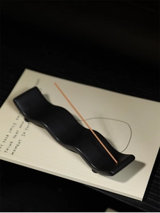 Détail du porte-encens en céramique noir mat en forme de vague sur un livre décoratif