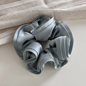Macro detail of ruffled grey-blue satin hair scrunchie with premium silk texture