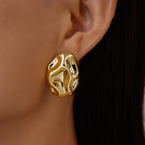 Detail of golden stud earrings with irregular lava texture and glossy metallic finish