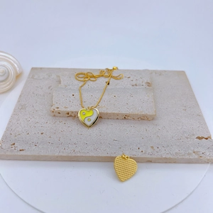 Detail of gold heart pendant with yellow and white enamel yin yang on stone slabs