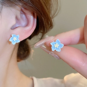Orecchini a perno a fiore blu menta con perla mostrati sull'orecchio e tenuti in mano