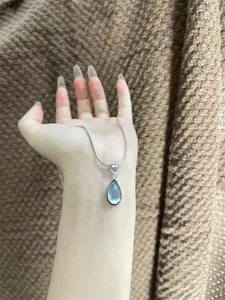 Detailed close-up of water drop shape blue pendant on a silver snake chain necklace