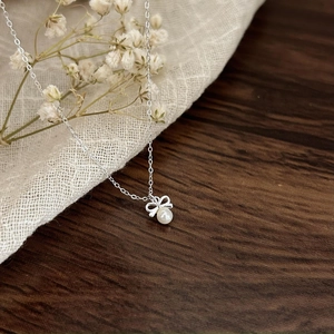 Detail of silver bow pendant with small white pearl on elegant dark wood table