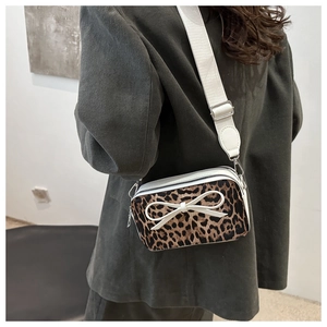 Detail view of leopard print crossbody bag with white bow and wide shoulder strap