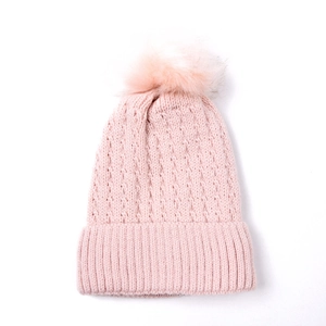 Close-up of pink cable knit beanie with fluffy faux fur pompom and ribbed cuff detail