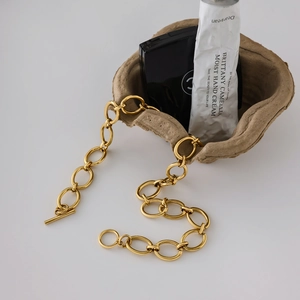 Détail du collier à gros maillons dorés avec fermoir toggle sur support minimaliste