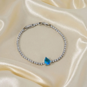 Detailed shot of a silver bracelet with a blue water-drop gemstone on golden silk