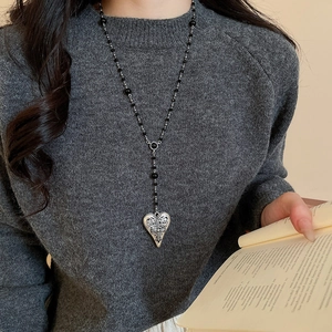 Détail du collier de perles noires avec pendentif coeur argenté et gravure de croix au cou