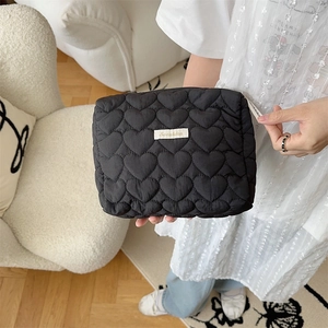 Close-up of black heart quilted makeup bag held by hand in a cozy indoor setting