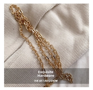 Detail view of refined multi-layered golden metal chain strap on beige textured fabric