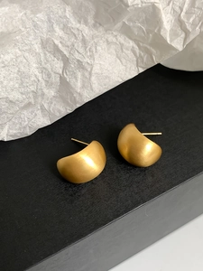 Macro detail of golden crescent earrings with a matte brushed metallic finish
