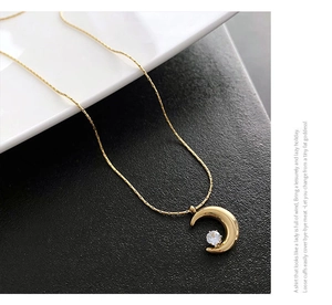 Detailed close-up of a gold crescent moon pendant necklace with a centered sparkling gemstone