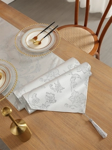 Silver-grey jute table runner with elegant floral patterns and tassels on a wooden table