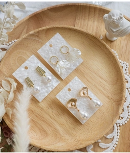 Detailed view of pearl earrings set on white textured card inside a wooden tray