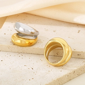 Close-up of minimalist gold and silver wide curved rings on a beige stone surface