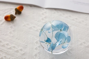 Close-up of a clear crystal ball containing preserved blue hydrangea petals on lace