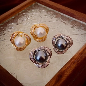 Close-up of pearl stud earrings with zircon twisted frames in gold and silver finish