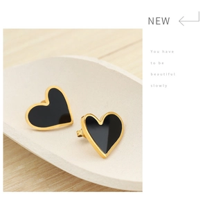 Detail of heart-shaped black and gold stud earrings on a white ceramic tray