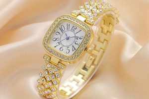 Gros plan d'une montre carrée dorée avec strass sur cadran et bracelet sur soie