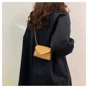 Detail of yellow crocodile pattern crossbody bag with golden chain strap on shoulder