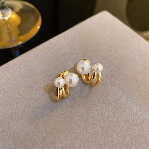Macro shot of gold-finished C-shape earrings featuring elegant white double pearls