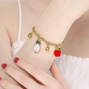 Detail of 18K gold fruit charm bracelet featuring dragon fruit and apple pendants