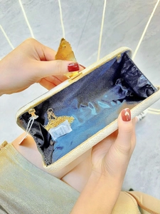 Detail of evening clutch bag showing off-white texture, leaf clasp and gold chain strap