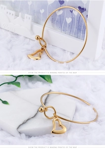 Close-up of gold minimalist bangle with hollow heart charm on white marble background