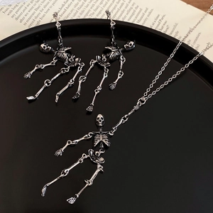 Close-up of gothic silver skull jewelry set with earrings and long necklace on a black plate