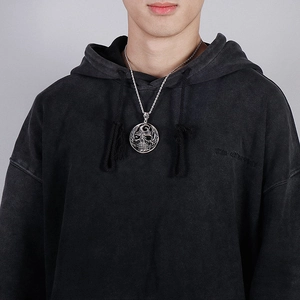 Close-up of a retro silver skull coin pendant on a twisted rope chain worn with a hoodie