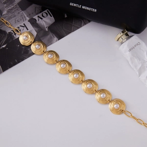 Macro detail of gold-tone chain bracelet with spiral textured charms and white pearls