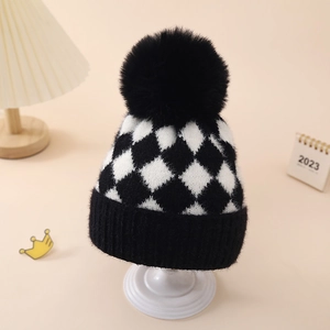 Detailed close-up of a winter knit baby hat featuring black and white argyle pattern and pompom