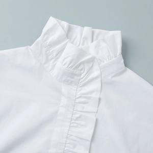 Macro shot of white stand collar blouse featuring detailed ruffles and pleated cotton fabric