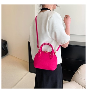 Fuchsia shell-shaped crossbody bag with crocodile embossing shown on a female model