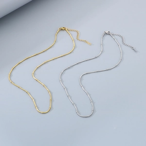 Adjustable stainless steel snake chain necklaces in gold and silver finishes on grey surface