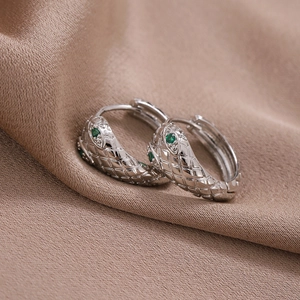 Silver snake hoop earring with green zircon eyes on luxurious brown satin backdrop