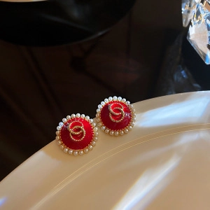 Close-up of red round earrings with pearl trim and interlocking golden logo detail