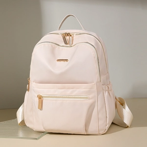 Detail of light pink nylon backpack featuring golden metal zippers and front pocket