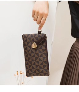 Close-up of a brown checkered wristlet bag with gold hardware held by a fashion model