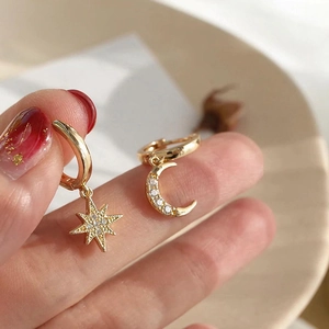 Close-up of asymmetrical gold hoop earrings with sparkling star and moon pendants