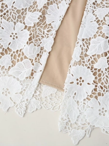 Gros plan détaillé de dentelle florale blanche avec doublure beige sur la robe élégante