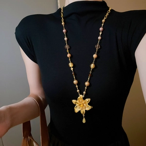 Détail d'un collier doré avec des perles et un grand pendentif en fleur évidée