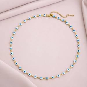 Close-up of golden chain necklace featuring blue evil eye beads on pink fabric