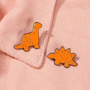Set di spille in smalto a forma di dinosauro arancione su sfondo di tessuto rosa