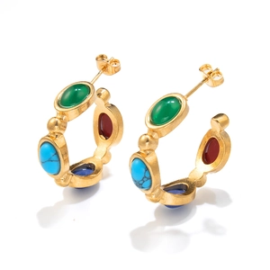 Detail of gold C-shaped hoop earrings with inlaid green, red, and blue gemstones