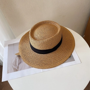 Overhead view of a flat top straw sun hat with black silk ribbon on a minimalist table